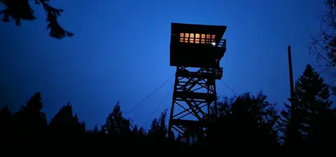 A fire lookout tower stands illuminated at night against a dark blue sky.