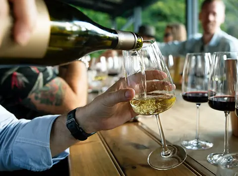 A person pouring white wine into a glass at a table.