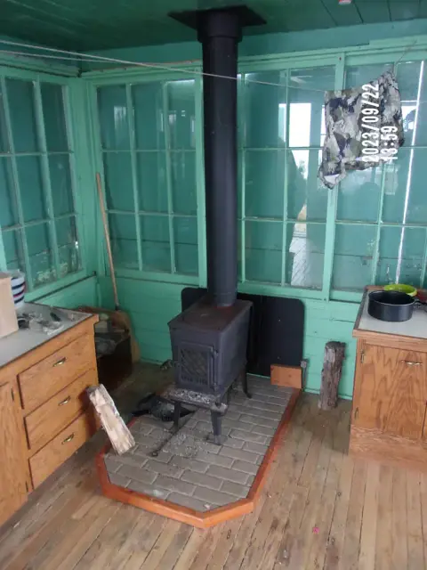 A wood-burning stove stands inside a room with green walls and large windows.