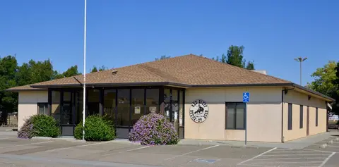 A single-story office building with a brown shingle roof and a parking lot in front.