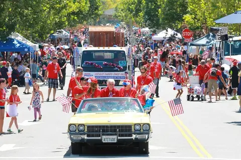 A parade moves down a street lined with people and booths.