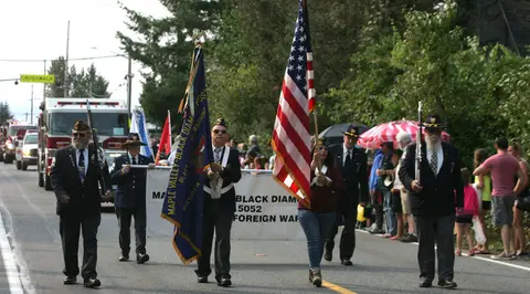 A color photograph of people carrying flags and rifles in a parade.