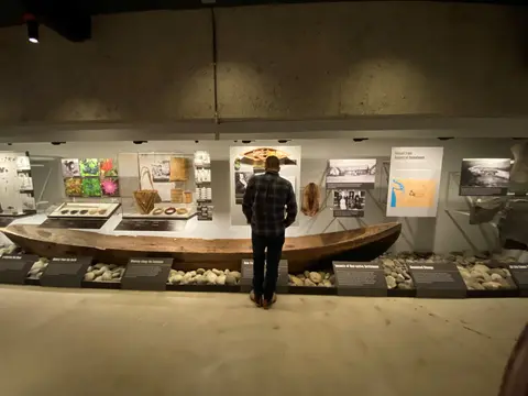 A visitor looks at a museum exhibit featuring a large wooden canoe and informative displays.