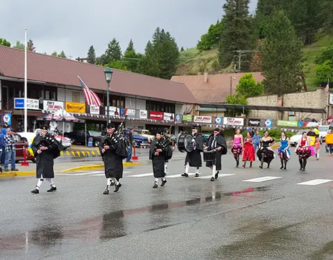 A group of people in traditional Scottish attire marching down a street during an outdoor event.