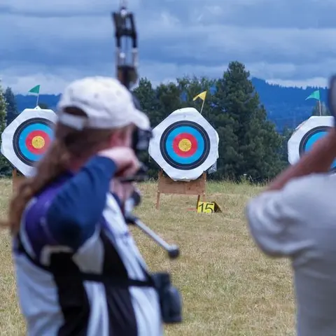 An archer aims at a target in a field.