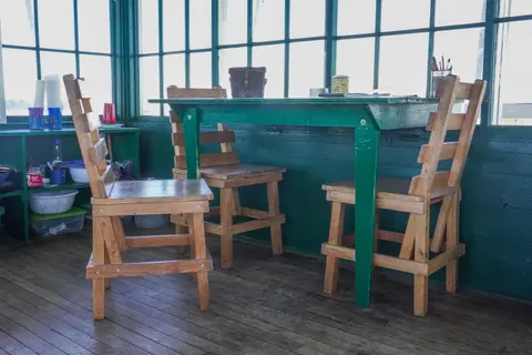 A green table with wooden chairs inside a room with large windows.