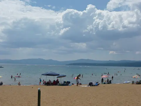 People enjoy a sunny day at a sandy beach with mountains in the background.