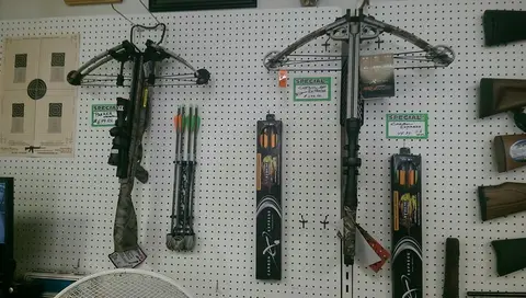 Two crossbows and arrows hang on a pegboard wall display inside a store.
