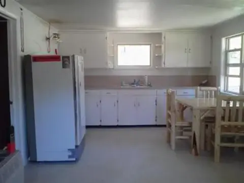 A photograph showing the interior of a kitchen with white cabinets and a refrigerator.