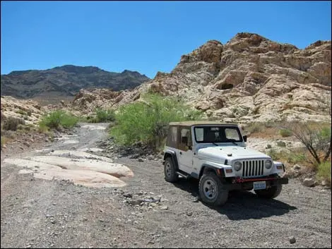 A white jeep is parked on a dirt track through a rocky desert landscape.