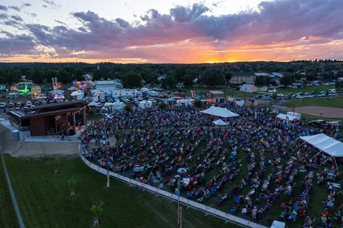 An aerial view shows a large crowd gathered for an outdoor concert at sunset.