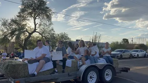 People ride on a hay bale trailer in a parade.