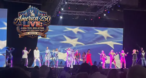 Performers on a stage with a large American flag backdrop and a graphic overlay.