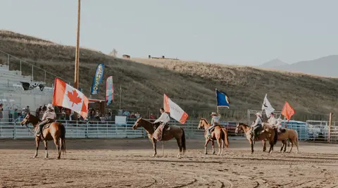 People on horseback carry flags in a dirt arena.