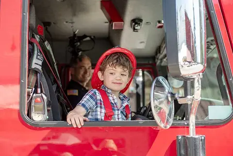 A child wearing a red helmet sits inside the cab of a fire truck.