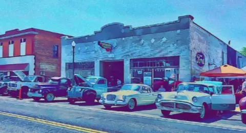 A row of vintage cars parked along a street in front of old brick buildings.