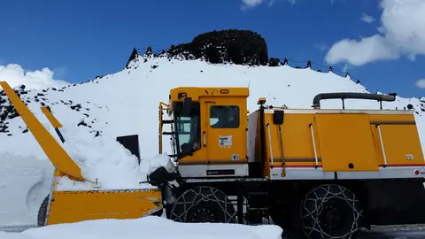 A yellow snow blower vehicle on a snow-covered mountain landscape.