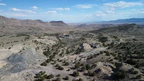 A high-angle view of a dry landscape with sparse vegetation, hills, and a road winding through the terrain.
