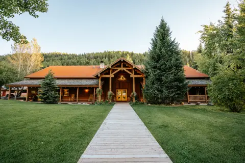 A wooden lodge building with a walkway leading up to it amidst trees and grass.
