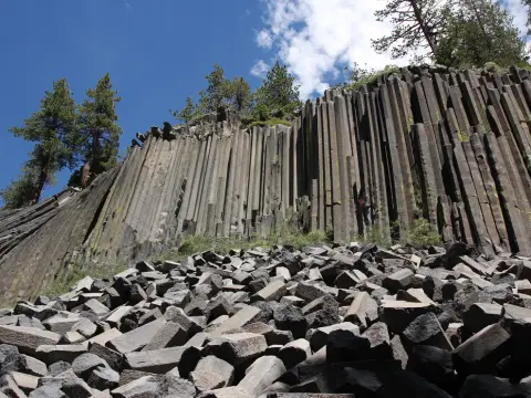 A tall cliff of columnar basalt rock formations with a pile of fallen hexagonal rocks at the base.