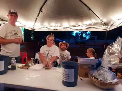 Four people stand behind a table under a white tent canopy with string lights.