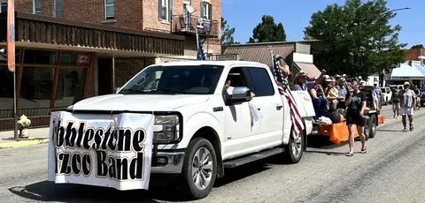 A white pickup truck pulls a parade float down a street.
