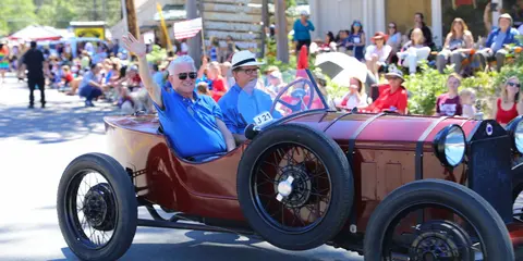 Two men ride in a vintage car during a parade.