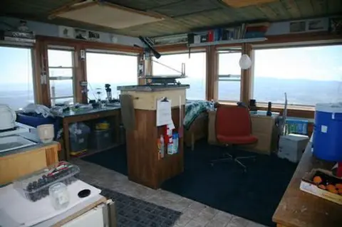 Interior of a fire lookout tower with windows offering views and a central table with equipment.