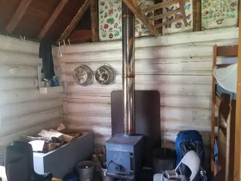 An interior view of a rustic log cabin with a wood-burning stove and bunk beds.