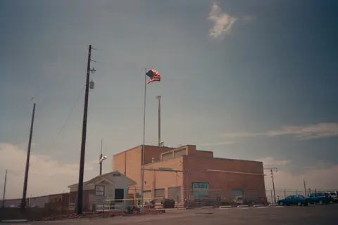 An exterior view of a low brick building with a flag flying out front.