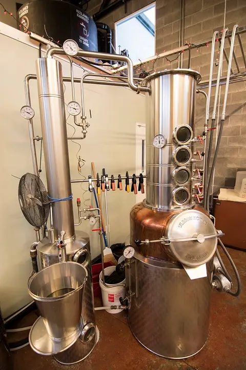 A stainless steel still apparatus is set up indoors for distillation.