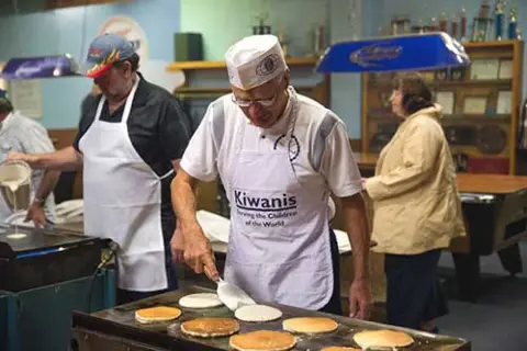 People cooking pancakes on a griddle inside a building.