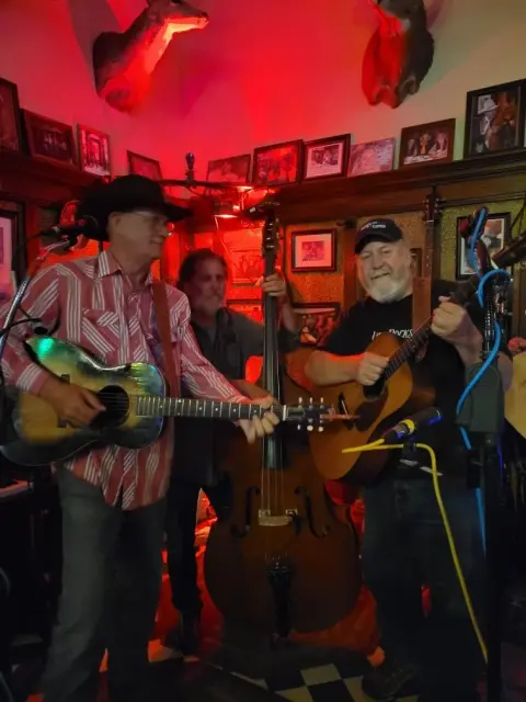 Three musicians perform with guitars and a double bass indoors.