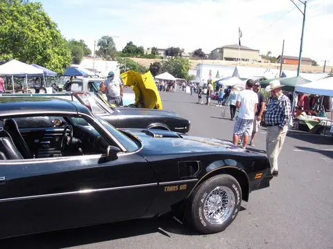 Classic cars are parked outdoors at a public gathering with tents and people.