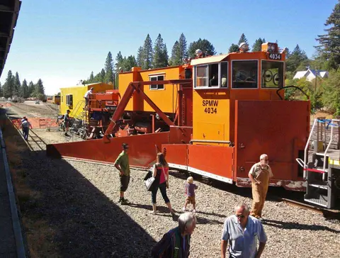 People stand near an orange railway maintenance vehicle on tracks.