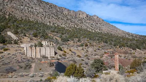 An outdoor view of historic mine ruins at the base of a barren mountain.