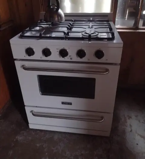 A white gas stove with a kettle on top stands indoors.