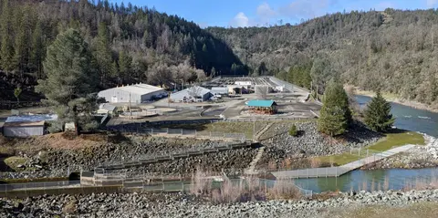 An industrial facility situated near a river in a mountainous landscape.