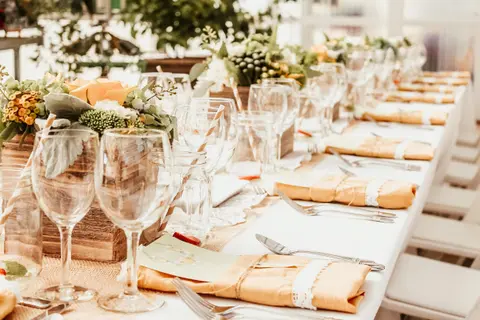 A long dining table is decorated with floral centerpieces, wine glasses, and place settings.