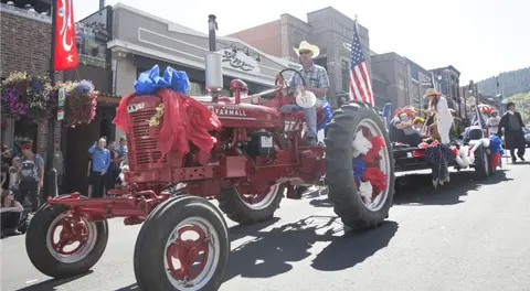 A red tractor is driven in a parade on a city street.