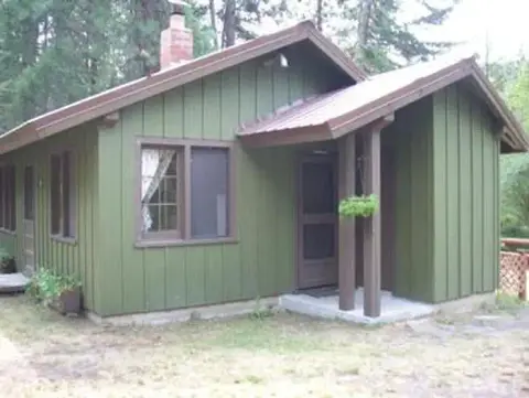 A green wooden cabin surrounded by trees.