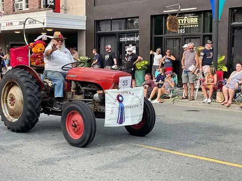 A man waves while driving a red tractor in a street parade.