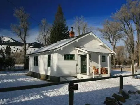 A white historic house stands in a snowy landscape under a blue sky.