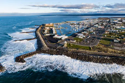 An aerial view of a coastal harbor protected by breakwaters with waves crashing against rocks.