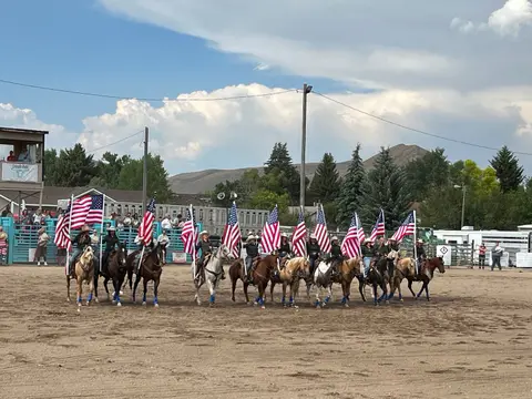 A line of horse riders carrying American flags in an arena.