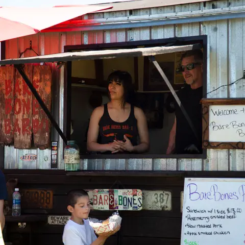 Two workers stand inside a food truck while a boy holds food in front.
