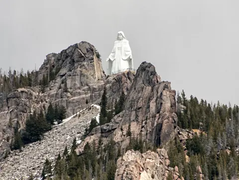 A large white statue of a figure stands atop a rocky mountain peak.