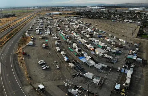 An aerial view shows a large parking lot or market filled with many vehicles and stalls.