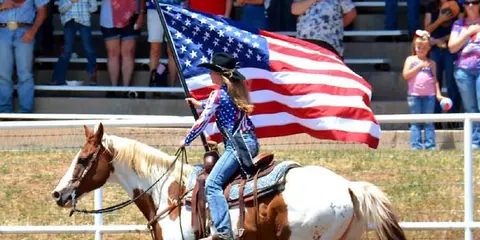 A rider on a horse carries an American flag past a crowd.