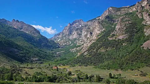 A valley surrounded by rocky mountains and green vegetation under a blue sky.